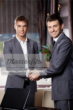 Two smiling business men shake hands each other at a meeting at restaurant