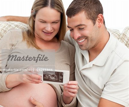 Proud future dad looking at an echography with his wife in the living-room