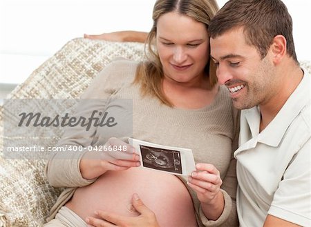 Lovely couple looking at an echography while relaxing in the living-room