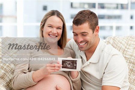 Beautiful pregnant woman showing her echography to her husband at home