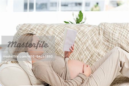 Concentrated pregnant woman reading a book lying on the couch at home