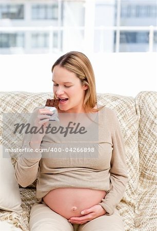 Joyful pregnant woman enjoing chocolate while resting on the sofa