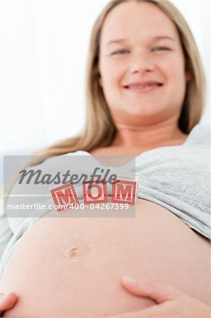 Close up of a woman having mom letters on her belly lying on a bed at home