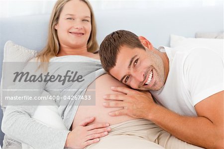 Portrait of a man listening the belly of his pregnant wife lying on their bed