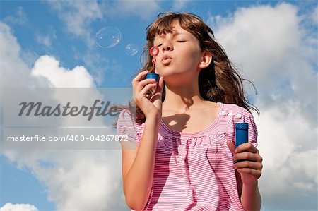 Teen girl blowing bubbles, on background of the sky