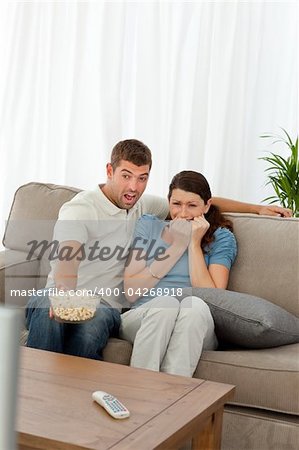 Terrified couple watching a horror movie in the living room at home