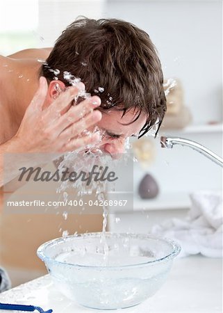 Attractive caucasian man spraying water on his face after shaving in the bathroom at home