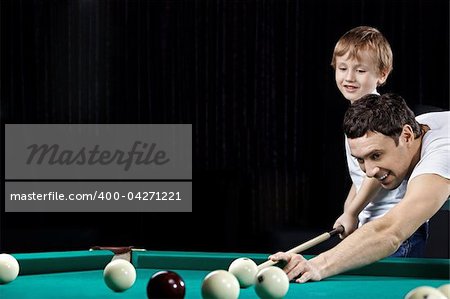 Young father and the son play billiards