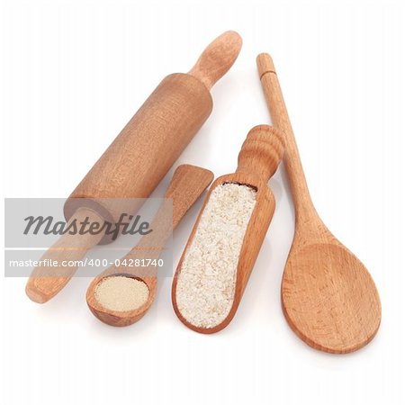 Rustic wooden baking utensils of scoop, spoons and rolling pin with yeast granules and wholegrain flour, over white background.