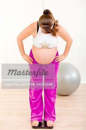 Pregnant woman standing on weight scale at living room