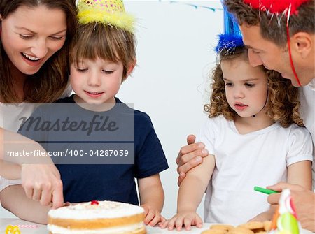 Mom and son cutting a birthday cake together in the kitchen with their family