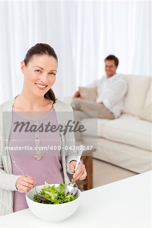 Pretty woman preparing a salad in the kitchen for her boyfriend sitting in the living room