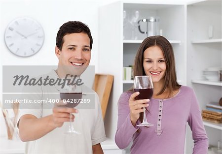 Young couple giving a toast with glasses of red wine in the kitchen