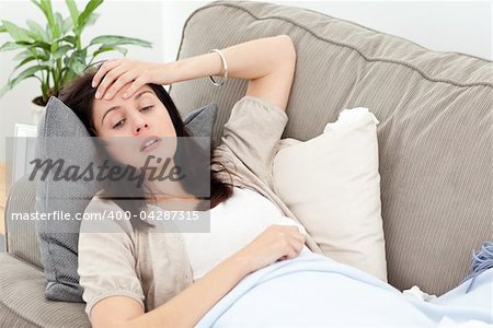 Indisposed woman feeling her temperature while resting on the sofa at home