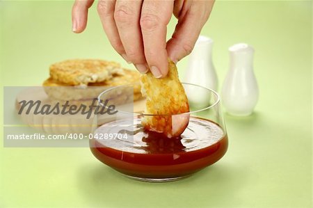 Dipping hash browns into a bowl of ketchup for breakfast.