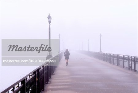 Landscape with  lonely lady crossing a bridge in the misty morning