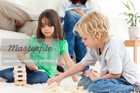 Cute brother and sister playing with dominoes on the floor in the living room