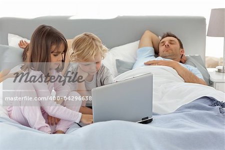 Attentive boy using a laptop with his sister while their parents are sleeping in the bed