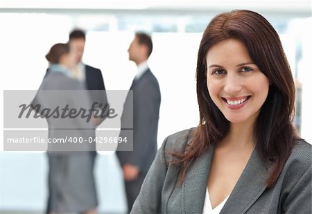 Happy businesswoman posing while her team discussing on the background
