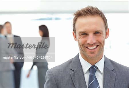 Happy businessman posing in front of his team while working on the background