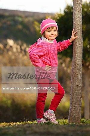 A picture of a young cute girl posing by the tree in the park