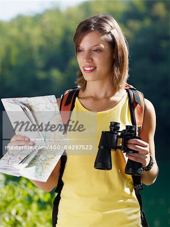 young caucasian female hiker reading map and holding binoculars. Vertical shape, waist up, front view