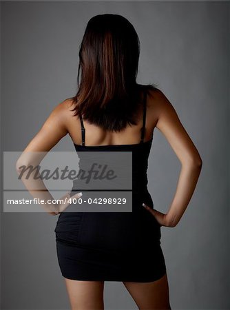 Young voluptuous Indian adult woman with long black hair wearing a black dress and blue coloured contact lenses on a neutral grey background. Mixed ethnicity