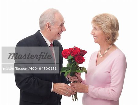 Gray-haired man in suit hands over a beautiful bouquet of red roses to an elderly woman, who is smiling as she accepts them. A gesture of love for Valentine's, birthday, or anniversary. Studio isolated on white.