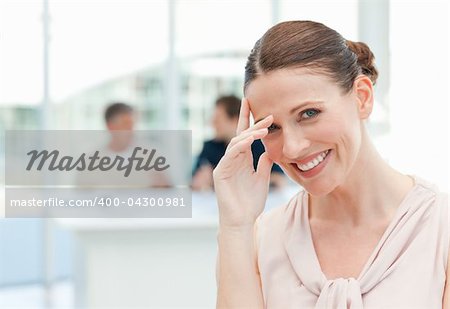 Smiling businesswoman looking at the camera while her coworkers are talking in the office