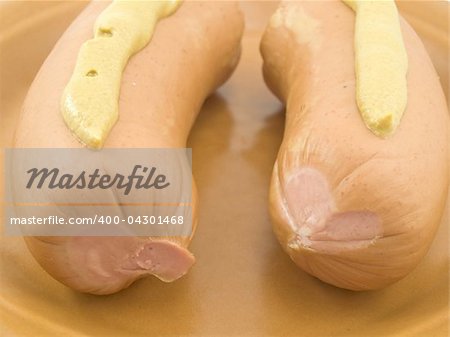 Two sausages with mustard are on a brown plate