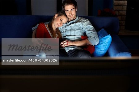 young heterosexual couple hugging on sofa and watching movie on tv at home. Horizontal shape, front view, copy space