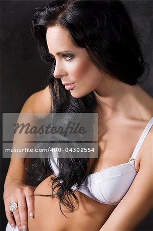 portrait of young pretty brunette with white bra against a dark background