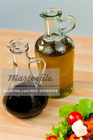 Bottles of olive oil and balsamic vinegar dressing with fresh lettuce tomato pepper olive red onion and feta cheese salad