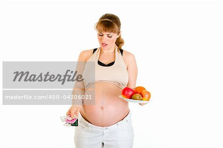 Thoughtful pregnant woman making choice between pills and fruits isolated on white