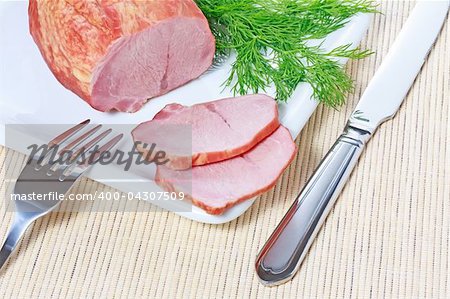 Smoked ham and dill on white plate with knife and fork on a bamboo mat