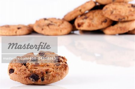 Close up of a chocolate chip cookie with a pile of chocolate chip cookies unsharp in the background on white.