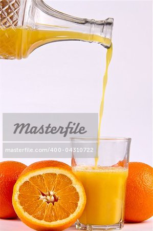 Orange juice being poured into a glass surrounded by orange fruits