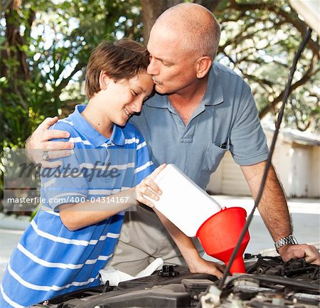 Loving father kisses his son as they work on the car engine together.