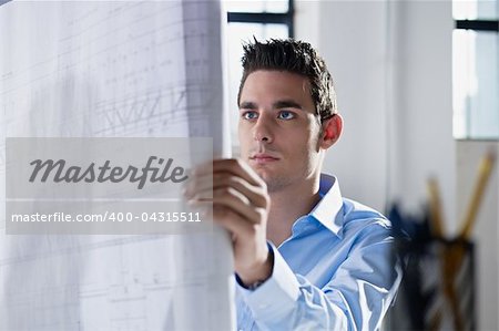 adult caucasian male architect examining blueprints. Horizontal shape, head and shoulders, side view