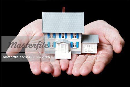 An isolated pair of womans hands holds a toy house.