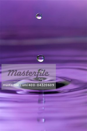 A purple abstract background of a close up of transparent water drops falling in water, making beautifull ripples and flowing waves in the surface and showing the pure energy it creates. Small depth of field.