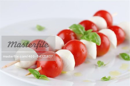 Cherry tomatoes and mozzarella on skewers, garnished with basil leaves and olive oil