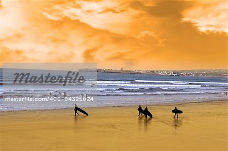 surfers walking on the beach in lahinch county clare ireland as the sun goes down