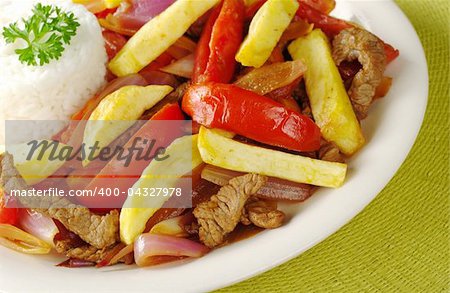A typical Peruvian dish called "lomo saltado" which is made of beef, onions, tomatoes and is accompanied by fried potatoes and rice (Selective Focus, Focus on the front of the dish)