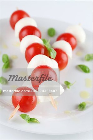 Cherry tomatoes and mozzarella on skewers, garnished with basil leaves and olive oil