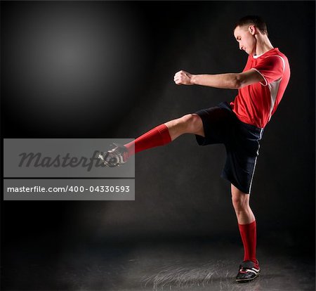 handsome soccer player kicks ball on black background