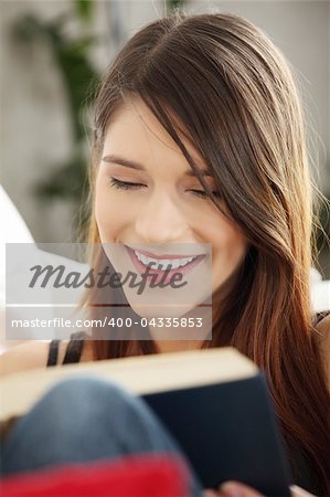 Beautiful woman reading a book, sitting on a sofa in a living-room