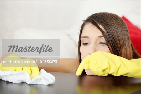 Tired young woman cleaning furniture table in yellow gloves