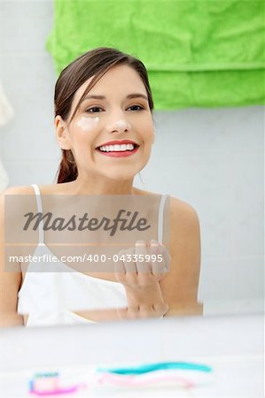 Beautiful woman applying cream on face at bathroom