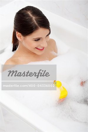 Beautiful young caucasian woman taking a bath with yellow duck.